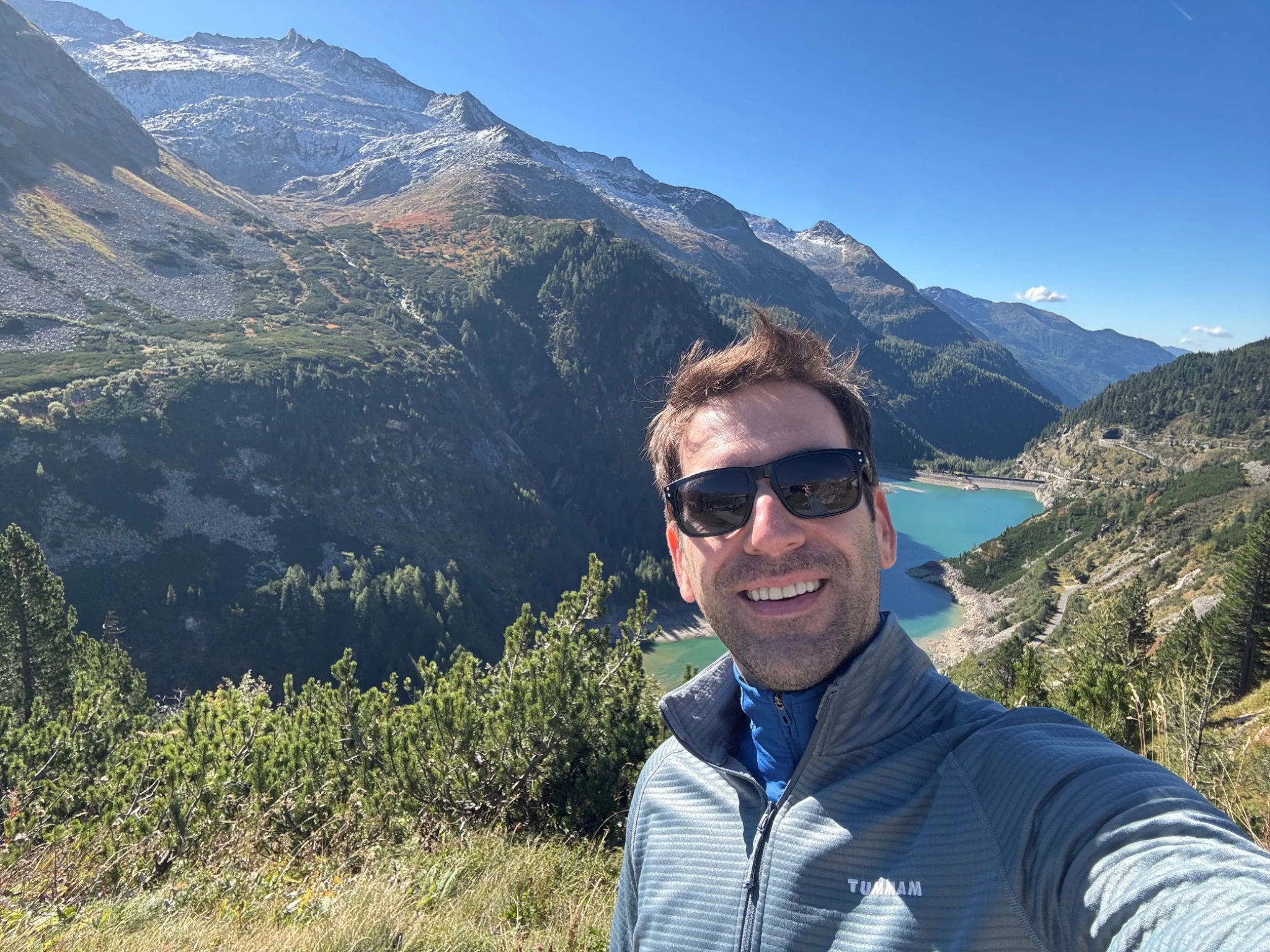 Christopher in the Alps, with a turquoise mountain lake behind him